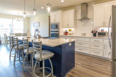 Kitchen featuring appliances with stainless steel finishes, an island with sink, white cabinets, wall chimney exhaust hood, and decorative light fixtures | Image 3