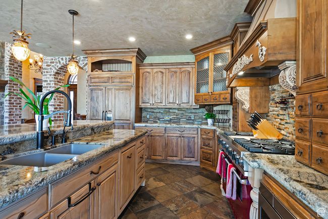 Kitchen with custom range hood, a sink, hanging light fixtures, brown cabinets, and decorative backsplash | Image 24