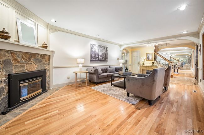 This 19.5' x 13' family room featuring a fireplace, detailed trim work, chair rail, and mirrored wall—anchored by hardwood floors and a wide architectural bay window. | Image 4