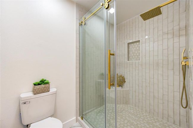 The primary bathroom features a luxurious walk-in shower, designed with modern elegance. The shower is equipped with a rain shower head, offering a spa-like experience with a gentle, soothing flow of water. The walls are beautifully finished with subway tile installed vertically, creating a sleek, contemporary look. The updated frameless glass door allows the design to shine, providing an open and airy feel. | Image 19