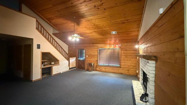Unfurnished living room featuring wooden ceiling, carpet floors, wood walls, a fireplace, and visible vents | Image 10