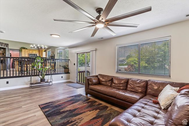 Living room with light wood-style floors, a textured ceiling, a ceiling fan, baseboards, and a chandelier | Image 9