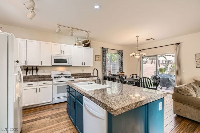 Kitchen featuring white appliances, blue cabinets, a sink, visible vents, and a notable chandelier | Image 9