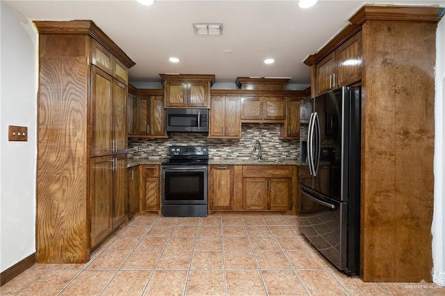 Kitchen featuring appliances with stainless steel finishes, light tile patterned floors, sink, backsplash, and light stone counters | Image 6