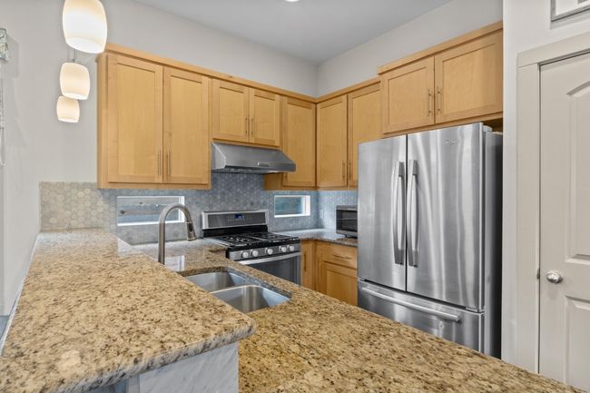 Kitchen featuring backsplash, under cabinet range hood, light stone countertops, stainless steel appliances, and a sink | Image 8