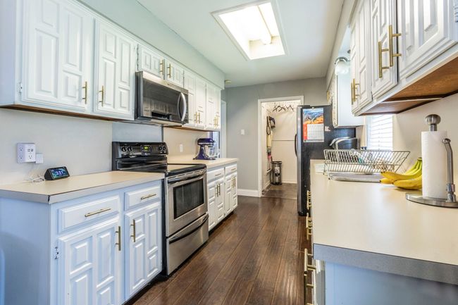 Kitchen featuring appliances with stainless steel finishes, white cabinets, dark wood finished floors, light countertops, and baseboards | Image 8