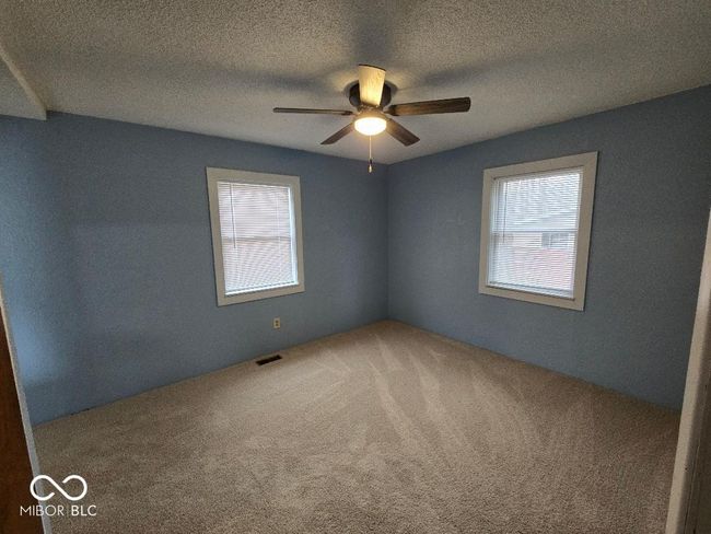carpeted empty room featuring a wealth of natural light, visible vents, a textured ceiling, and ceiling fan | Image 26