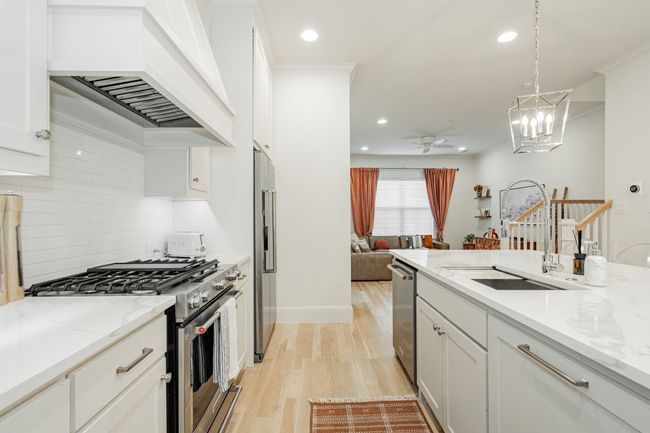 Kitchen featuring light wood-type flooring, white cabinets, custom exhaust hood, a sink, and stainless steel appliances | Image 7