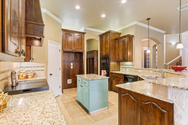 Kitchen with visible vents, light stone countertops, arched walkways, black appliances, and a sink | Image 15