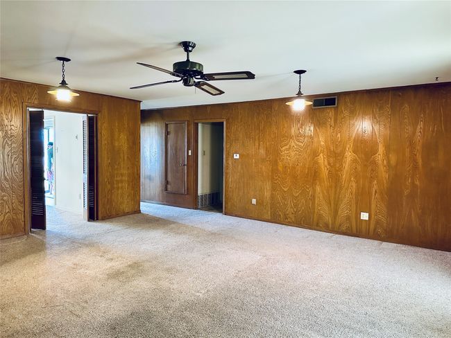 Empty room featuring carpet, visible vents, wood walls, and ceiling fan | Image 4
