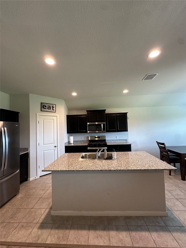Kitchen featuring stainless steel appliances, a sink, a center island with sink, visible vents, and dark cabinets | Image 13