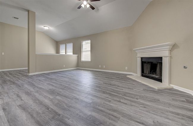 Unfurnished living room with a ceiling fan, vaulted ceiling, a fireplace with raised hearth, and wood finished floors | Image 5