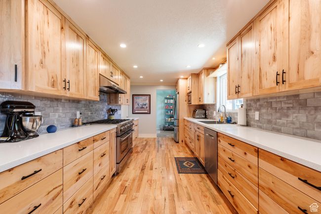 Kitchen featuring light brown cabinetry, under cabinet range hood, a sink, light wood-type flooring, and appliances with stainless steel finishes | Image 8