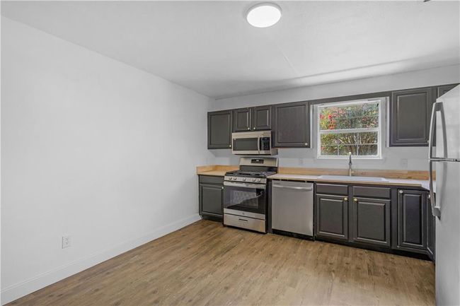 Kitchen featuring wood finished floors, baseboards, a sink, light countertops, and appliances with stainless steel finishes | Image 9