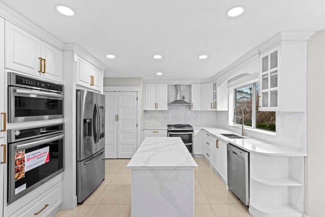 Kitchen featuring wall chimney range hood, a center island, open shelves, stainless steel appliances, and a sink | Image 10