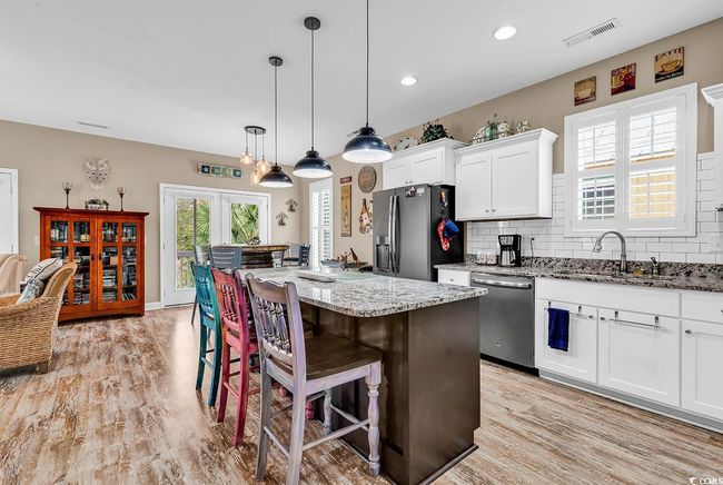 Kitchen featuring visible vents, stainless steel appliances, white cabinetry, a sink, and a breakfast bar area | Image 11