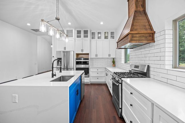 Kitchen with appliances with stainless steel finishes, custom exhaust hood, blue cabinetry, recessed lighting, and white cabinetry | Image 9
