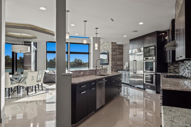 Kitchen with dark cabinets, light stone countertops, decorative light fixtures, appliances with stainless steel finishes, and light tile patterned floors | Image 47