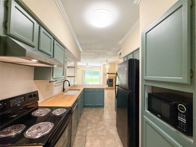 Kitchen with green cabinetry, black appliances, a peninsula, range hood, and crown molding | Image 4