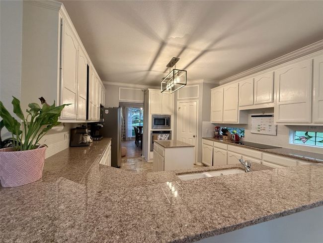 Kitchen featuring a sink, stone countertops, stainless steel appliances, white cabinetry, and tasteful backsplash | Image 9