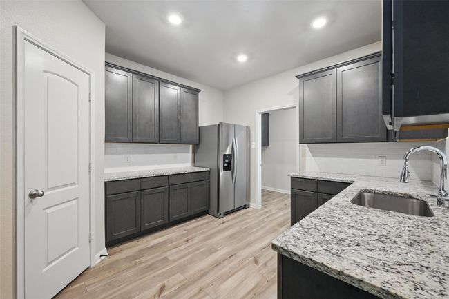 Kitchen featuring tasteful backsplash, stainless steel refrigerator with ice dispenser, a sink, light stone countertops, and light wood-style flooring | Image 7
