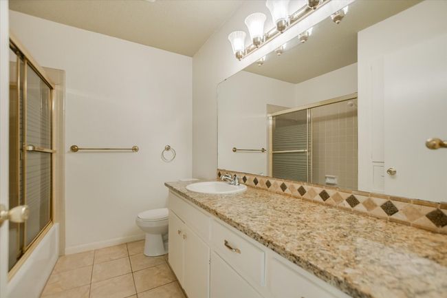 Bathroom with toilet, tile patterned flooring, vanity, enclosed tub / shower combo, and baseboards | Image 13