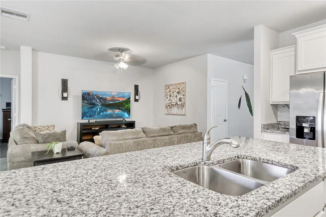 Kitchen featuring sink, light stone counters, white cabinetry, stainless steel fridge with ice dispenser, and ceiling fan | Image 17