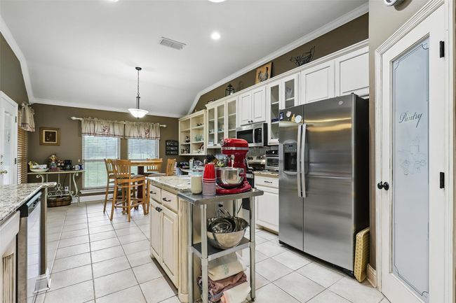 Kitchen with stainless steel appliances, open shelves, ornamental molding, tasteful backsplash, and light tile patterned floors | Image 11