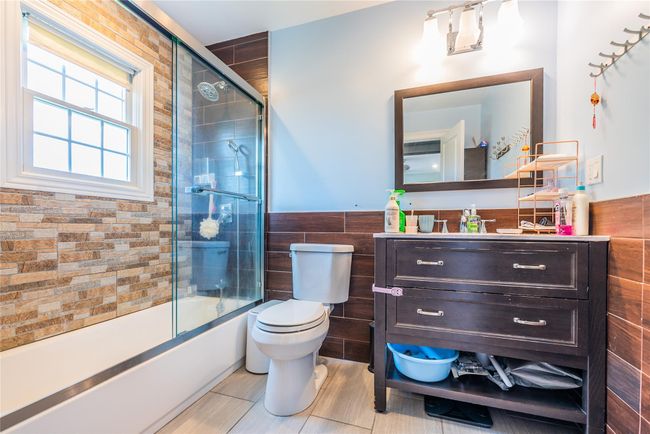 Full bathroom with tile walls, toilet, vanity, combined bath / shower with glass door, and a wainscoted wall | Image 8