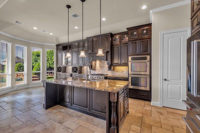 Equipped with sleek stainless steel appliances, including double ovens that make cooking and entertaining effortless. Elegant pendant lighting hangs above a large granite countertop island, offering ample workspace and seating. | Image 9