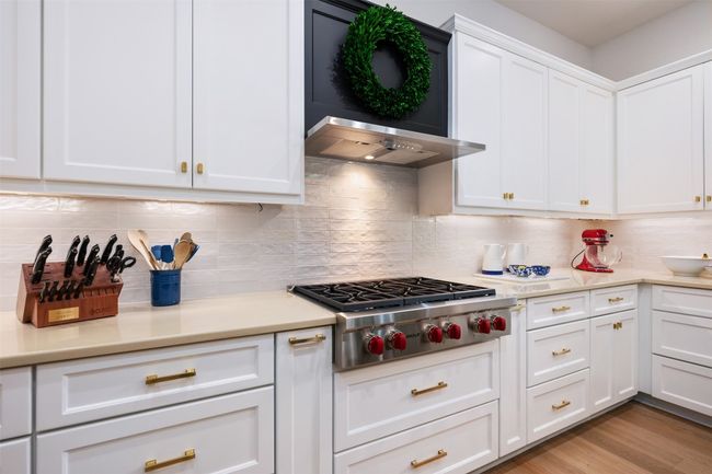 Kitchen with Wolf stainless steel gas cook top, white cabinetry, light countertops, decorative backsplash, and light wood-style flooring. Restoration hardware throughout the home. | Image 10