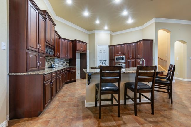 Kitchen featuring stainless steel appliances, arched walkways, crown molding, a breakfast bar area, and decorative backsplash | Image 6