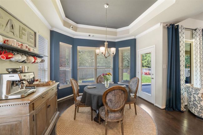 This cozy breakfast nook features a stylish tray ceiling and abundant natural light from large windows. It includes a chic coffee bar and an elegant chandelier over a round table, creating a welcoming atmosphere perfect for meals or entertaining. | Image 11