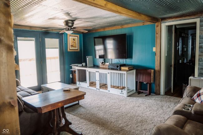 living room with carpet flooring, a ceiling fan, wooden walls, and beam ceiling | Image 31