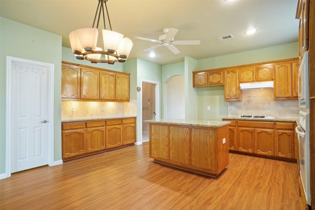 Kitchen featuring light wood-type flooring, under cabinet range hood, ceiling fan, visible vents, and brown cabinetry | Image 11