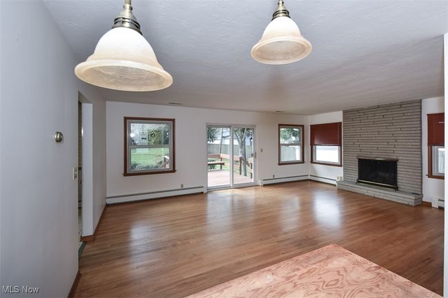 Unfurnished living room featuring baseboard heating, a baseboard radiator, wood finished floors, and a fireplace | Image 16