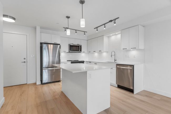 Kitchen with appliances with stainless steel finishes, a sink, light wood-style flooring, white cabinets, and a center island | Image 9