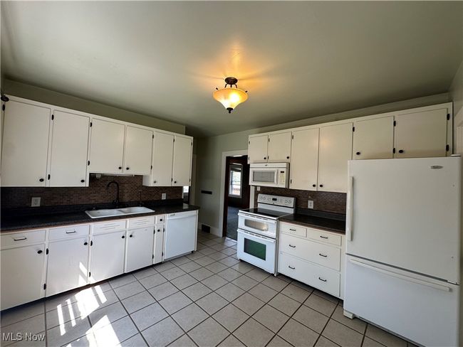 Kitchen featuring dark countertops, tasteful backsplash, a sink, white appliances, and white cabinetry | Image 4