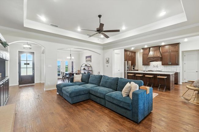 Living room with arched walkways, a tray ceiling, dark wood-type flooring, ceiling fan, and ornamental molding | Image 11