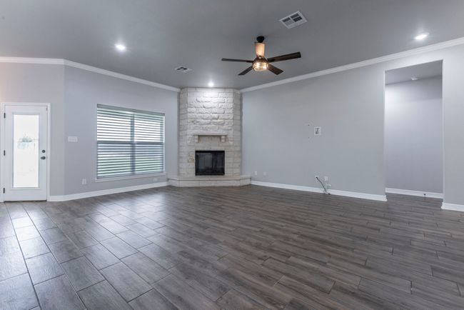 Unfurnished living room featuring ceiling fan, dark wood-style floors, crown molding, a stone fireplace, and recessed lighting | Image 6