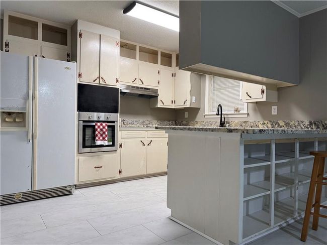 Kitchen with white refrigerator with ice dispenser, under cabinet range hood, a peninsula, ornamental molding, and a kitchen bar | Image 8