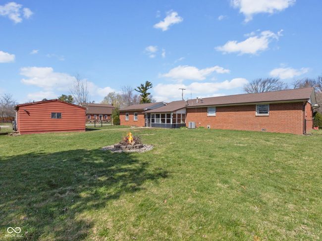 rear view of property featuring a sunroom, central air condition unit, brick siding, a fire pit, and a yard | Image 31