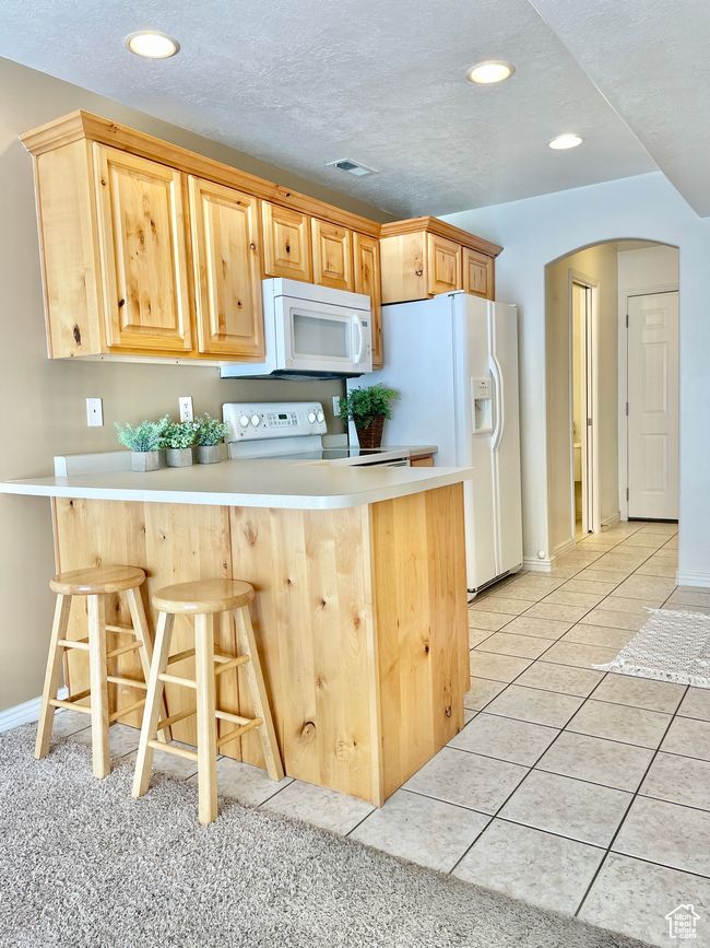 Kitchen featuring white appliances, arched walkways, a peninsula, a breakfast bar area, and light brown cabinets | Image 8
