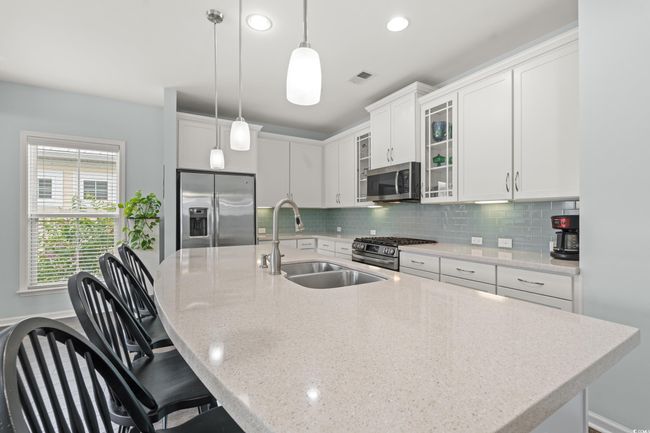 Kitchen with appliances with stainless steel finishes, a sink in the large island, dark wood-style flooring, glass insert cabinets, light stone counters, recessed lighting and under cabinet lighting. | Image 26