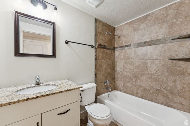 Bathroom with a textured ceiling, toilet, vanity, and washtub / shower combination | Image 10