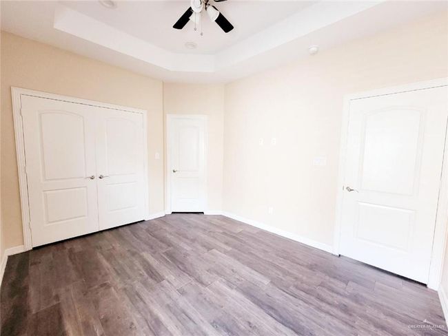 Unfurnished bedroom featuring wood finished floors, a tray ceiling, ceiling fan, and a closet | Image 16