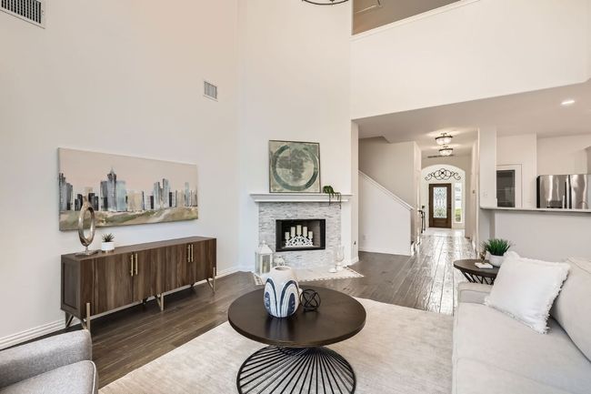 Living area with wood-type flooring, a towering ceiling, baseboards, and a fireplace | Image 4