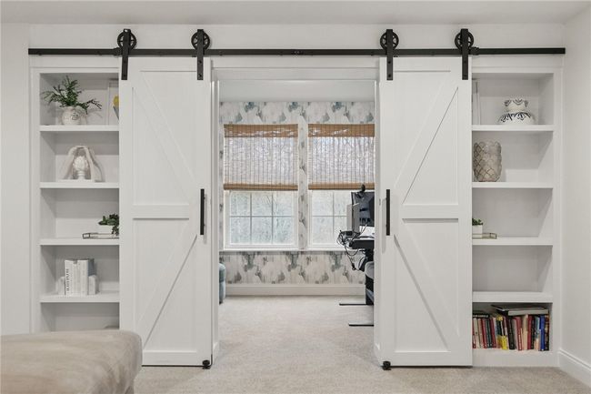 Stylish and functional bonus room tucked behind sliding barn doors with built-in shelving. Perfectly suited as a private home office, study, or creative space, featuring large windows that fill the room with natural light and offer serene wooded views. | Image 32
