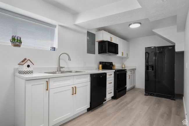 Kitchen with black appliances, a textured ceiling, electric panel, light wood finished floors, and white cabinets | Image 7