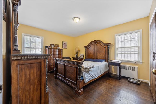 Bedroom featuring radiator heating unit, baseboards, dark wood finished floors, and multiple windows | Image 7